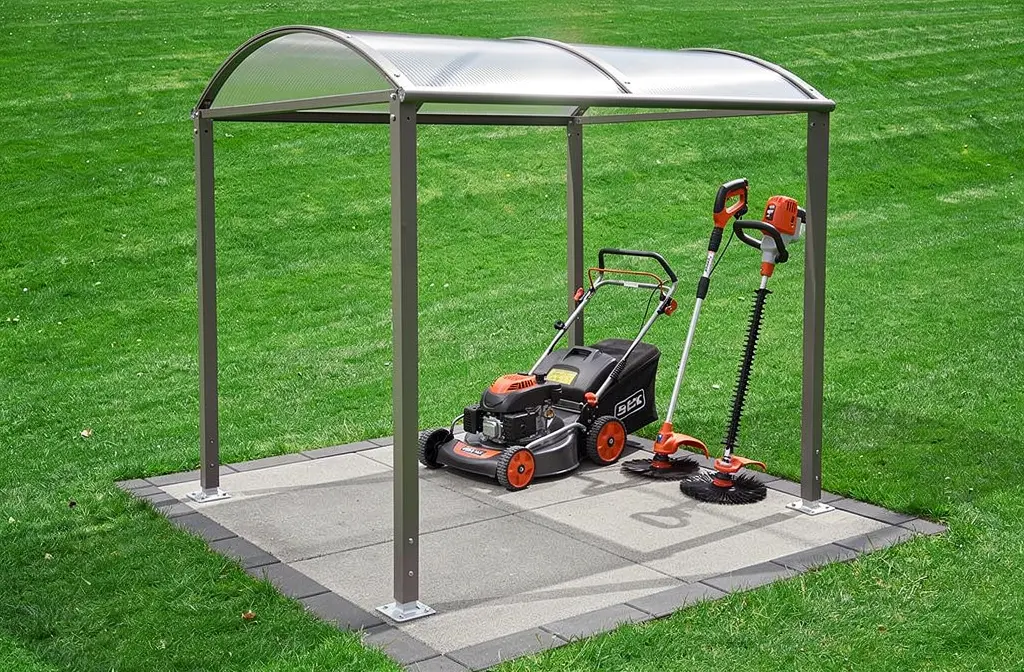 Abri de rangement pour outils d’espace vert avec tondeuse et outils de jardinage sur une base de pavés, cadre métallique et toit transparent. matériel espace vert professionnel.