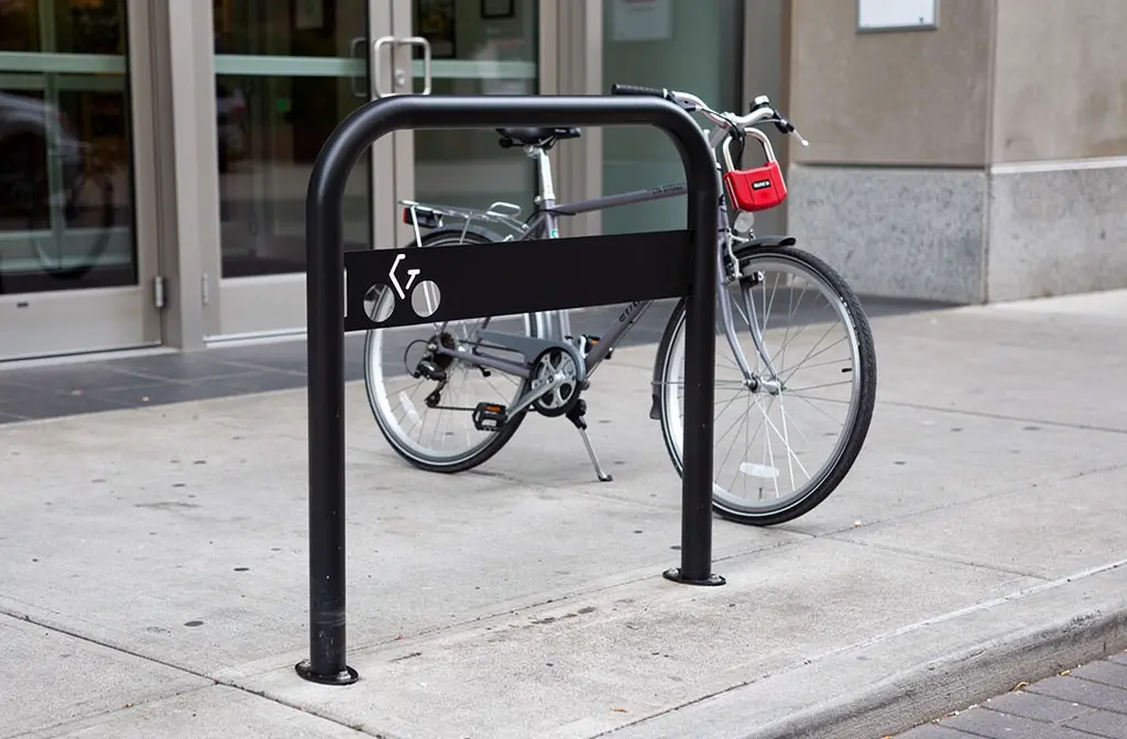 Arceau anti-stationnement vélo en métal noir entourant un cadre de stationnement, vélo attaché à l’arceau près d’un bâtiment urbain.