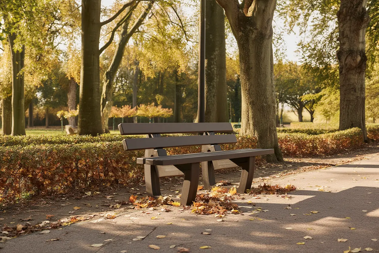 Banc public en plastique recyclé dans un parc ombragé, entouré d’arbres et de feuilles d’automne, sans entretien apparent.