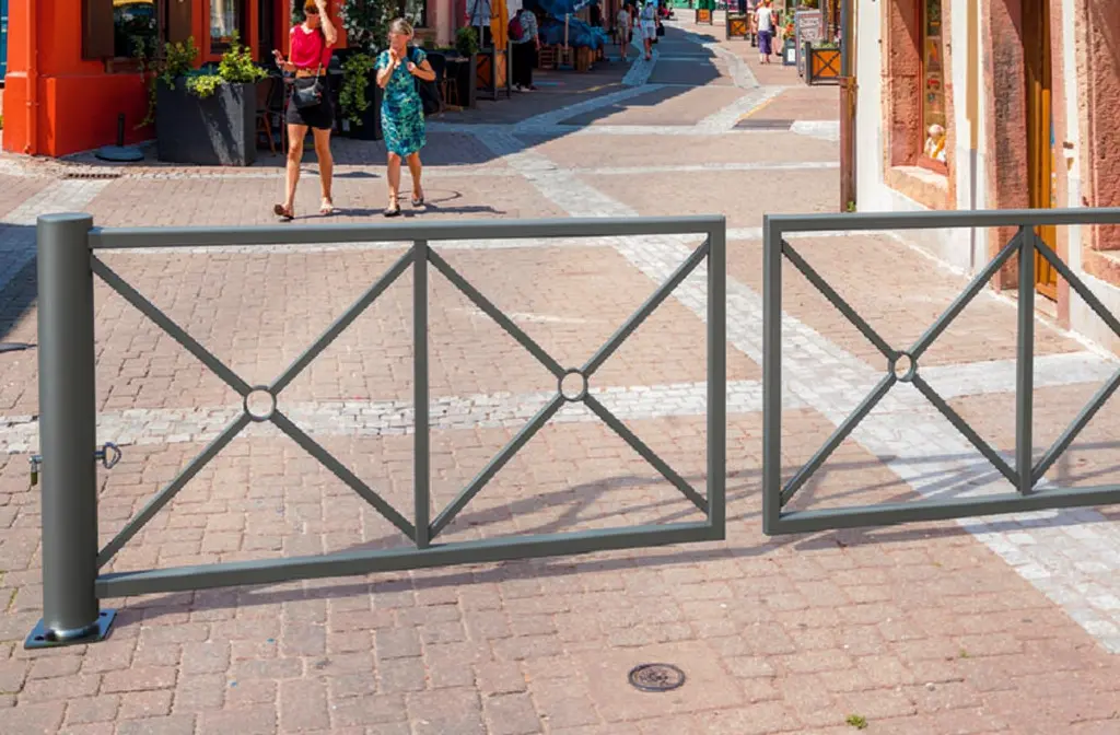 Barrières amovibles installées sur une rue piétonne pavée, séparant une zone piétonne avec des passants en arrière-plan. Intègre subtilement le contexte de sécurité routière et d’obligation pour les communes. Nouvelle loi sur les passages piétons 2026.